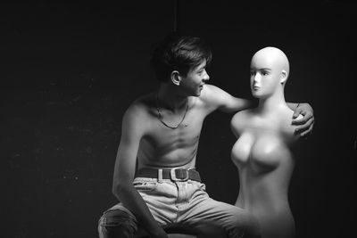 Young man looking at mannequin against black background