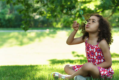 Young woman blowing bubbles while sitting on field