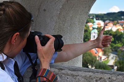 Woman photographing through camera while gesturing thumbs up sign outdoors