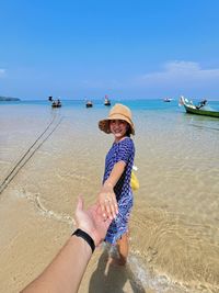 Cropped hand of man holding woman on shore at beach during sunny day