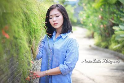 Young woman looking away while standing against plants