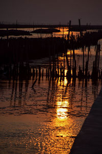 Silhouette wooden posts in lake against sky at sunset