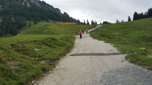 People walking on road by mountain against sky