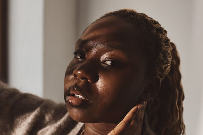 Young woman touching ear against wall