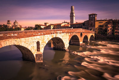 Arch bridge over river during sunset