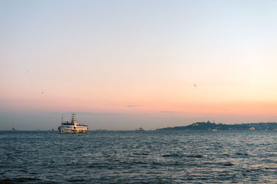 Boat sailing in sea against clear sky during sunset