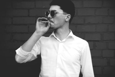 Young man smoking while standing against brick wall
