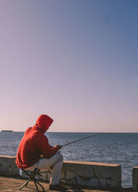 Man sitting on seat against sea against clear sky