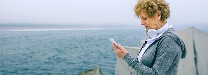 Man holding mobile phone while standing by sea