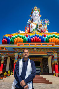 Young man praying in front of buddhist colorful goddess statue with blue sky at morning