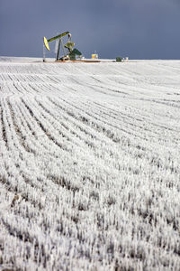 Mid distance view of pumpjack at oil industry on field against sky during winter