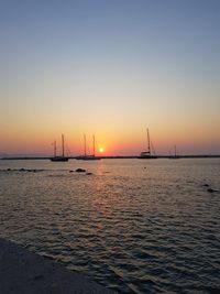 Sailboats sailing in sea against sky during sunset