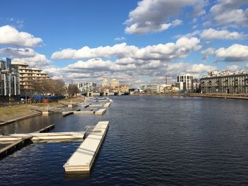 City by river against cloudy sky