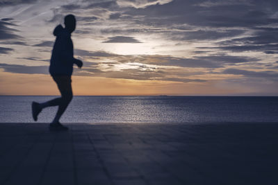 Silhouette woman standing on beach against sky during sunset