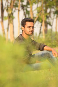 Side view of thoughtful young man looking away while sitting on grassy field in park