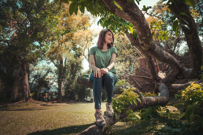 Low angle view of woman sitting on tree trunk