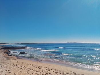 Scenic view of beach against clear blue sky