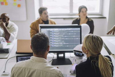 Rear view of professor discussing with student over computer at desk in innovation lab