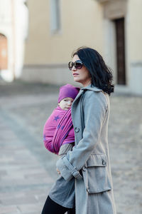 Woman carrying son in scarf on walkway