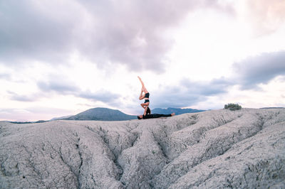 Side view of woman balancing upside down on arms of man during acroyoga session in mountains