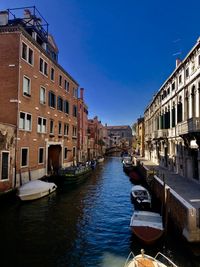 Boats moored in canal amidst buildings in city against sky