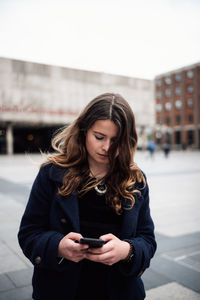 Young woman using phone while standing on snow