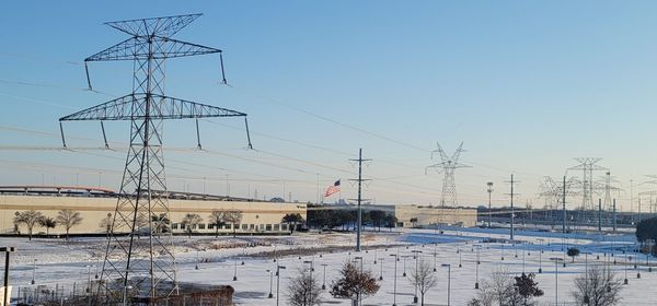 Electricity pylon on snow covered landscape against sky