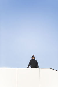 Rear view of woman standing by built structure against blue sky