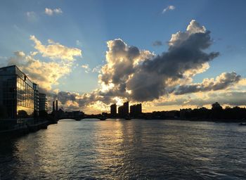 Silhouette city by river against sky during sunset