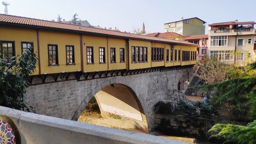 Arch bridge over river by buildings against sky
