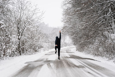 Rear view of man walking and jumping on snow covered road