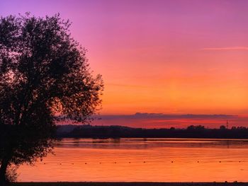 Silhouette trees by lake against romantic sky at sunset