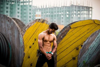 Shirtless man standing by wood in city