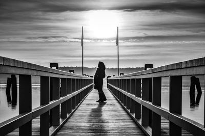 Silhouette woman walking on footbridge against sky