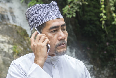 Thoughtful man talking on phone while sitting against waterfall