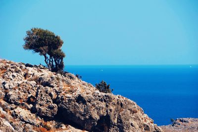 Rocks by sea against clear blue sky