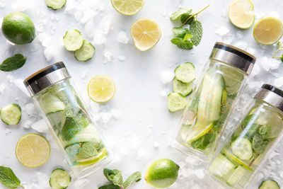 Bottles of infused cucumber water with ingredients and ice all around.