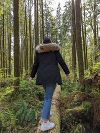 Girl walking on a log through a green forest.