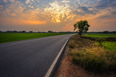 Road by field against sky during sunset