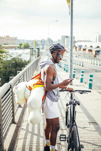 Happy bicycle courier with cell phone and teddy bear