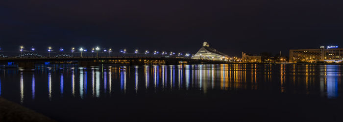 Illuminated buildings by river against sky at night