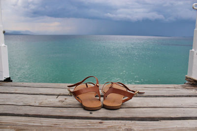 Sandals on pier by sea against sky