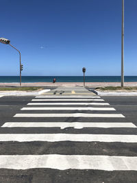 Zebra crossing on road by sea against clear sky