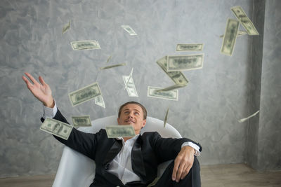 Businessman holding money while sitting against wall