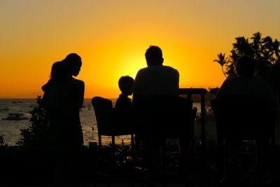 Silhouette people sitting on chair against sea during sunset