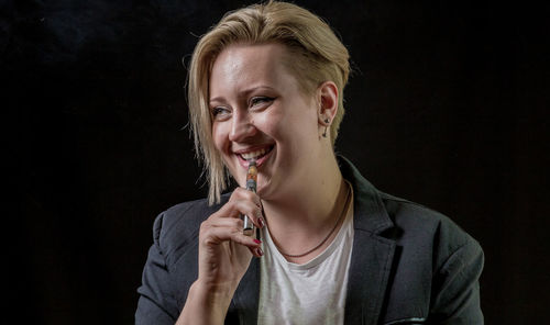 Portrait of smiling young woman against black background