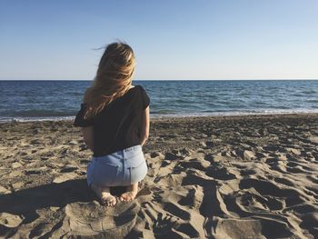 Rear view of girl sitting on beach against clear sky