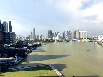 Modern buildings by river against sky in city