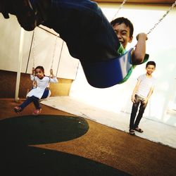 Siblings swinging with boy in playground