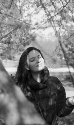 Smiling woman with eyes closed standing by tree